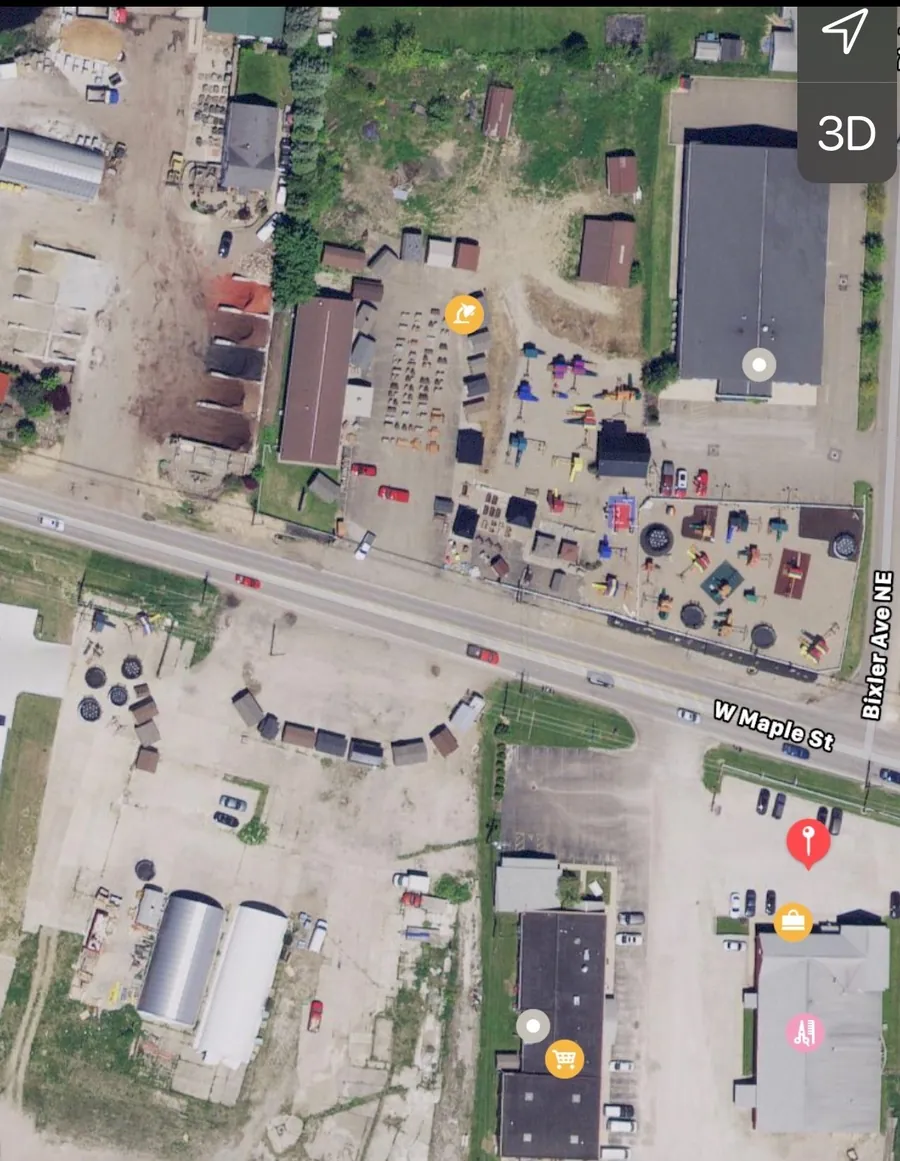 Older aerial view of West Maple Street in Hartville, Ohio: a small curved row of display sheds on a mostly empty gravel lot south of the road